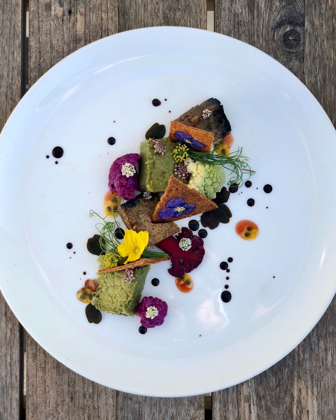 A vibrant plant-based dish plated with edible flowers, herbs and roasted vegetables in warm light